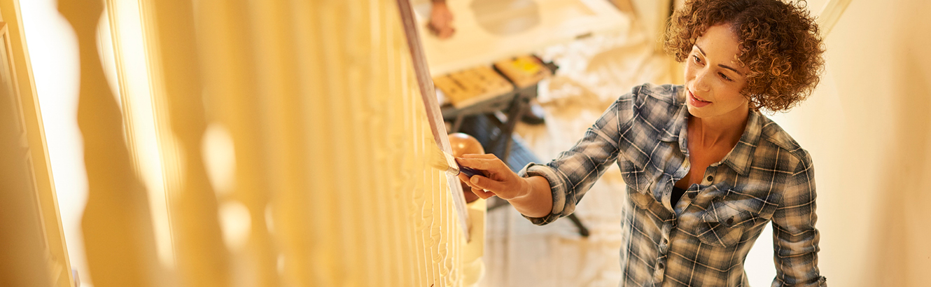A middle-aged woman painting a staircase a pale yellow.