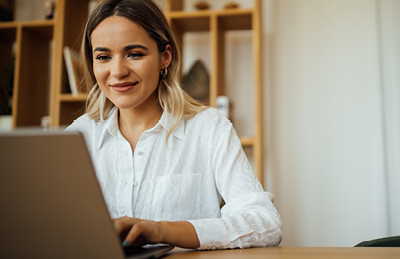 Young woman smiling while using a laptop at home.