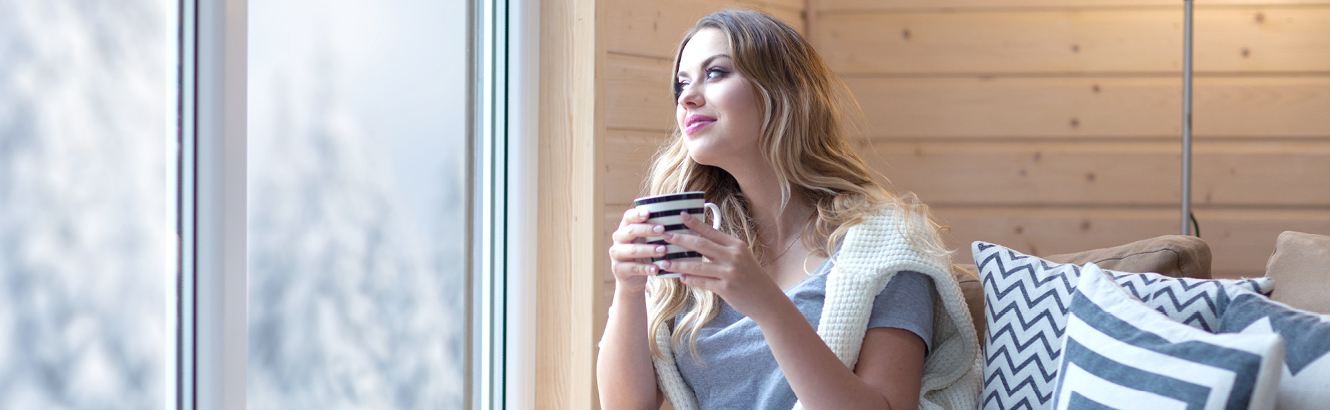 woman drinking coffee at home, gazing out the window