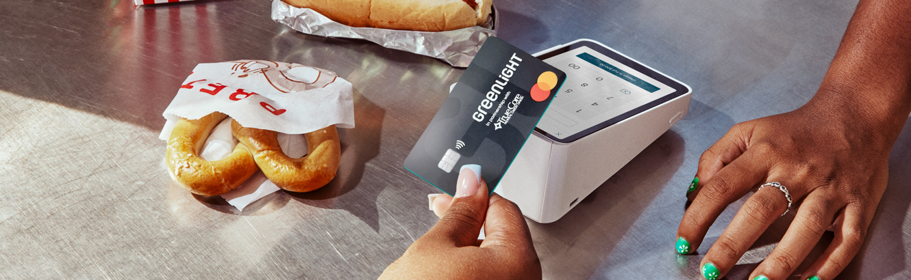 Closeup of a teen, at a movie theater, paying for snacks with a Greenlight branded debit card.